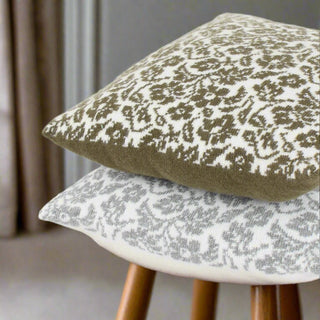 Two square floral patterned wool cushions on a wooden stool, one with a darker green floral pattern and the other with a lighter white floral pattern, both with envelope style closures.