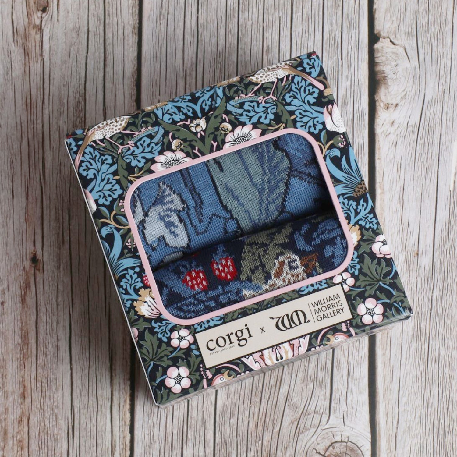 A box of Men's William Morris socks with a floral and animal pattern, including pairs with bird and berry motifs and swirling foliage designs.