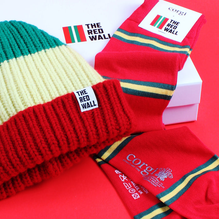 A set of Red Wall branded merchandise including a beanie hat and socks, with the logo featuring red, yellow, and green stripes, presented on a red background.