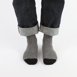 Gray socks worn with dark jeans on a white background