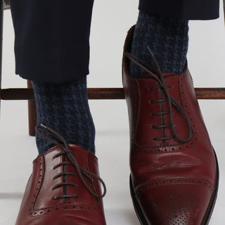 A pair of men's formal houndstooth merino wool socks in blue, showing the pattern and texture, worn with brown leather shoes.