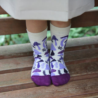 Child wearing white socks with purple mushroom pattern sitting on a wooden bench.