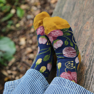 Child wearing floral socks with yellow toes and heels, sitting against a wooden post outdoors.