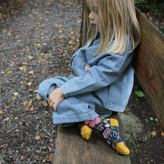 Child wearing a blue striped outfit sitting on a wooden bench outdoors.