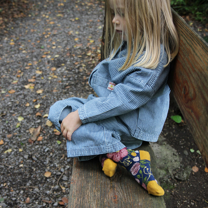 Child wearing a blue striped outfit sitting on a wooden bench outdoors.