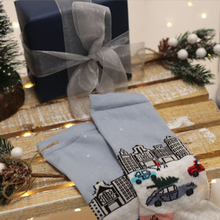 A pair of women's socks with a Christmas in the city scene design, featuring a snow-covered street, buildings, and decorative elements.
