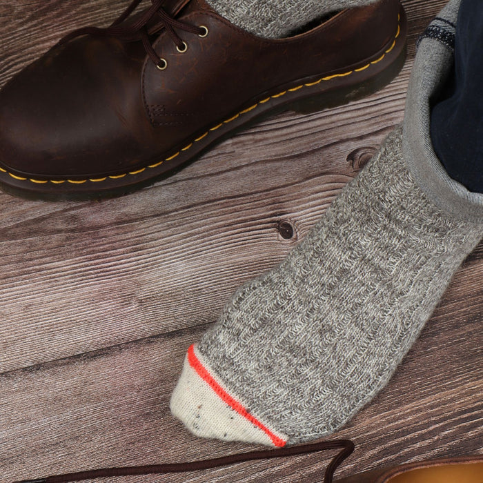 A pair of men's striped cuff British wool socks in gray, displayed alongside a brown boot.