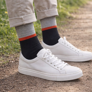 White sneakers worn with gray socks featuring navy and orange stripes on a natural background.