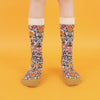 A pair of patterned cotton socks featuring a floral design with roses and leaves, and gold accents on the heel and toe, displayed against a yellow background.
