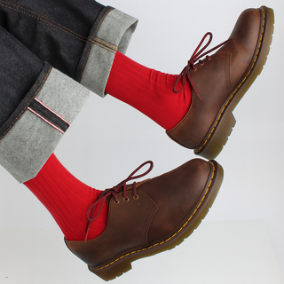 Brown shoes with red socks worn by a person on a white background