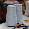 Two spools of light blue yarn on a table with scissors and other tools in the background.