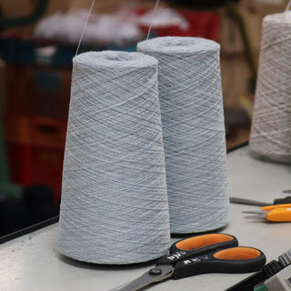 Two spools of light blue yarn on a table with scissors and other tools in the background.
