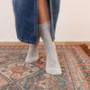 A pair of plain grey cotton socks worn with denim jeans, standing on a patterned carpet.