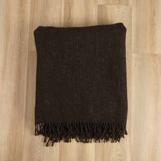 Dark brown woven blanket with fringes on a wooden floor