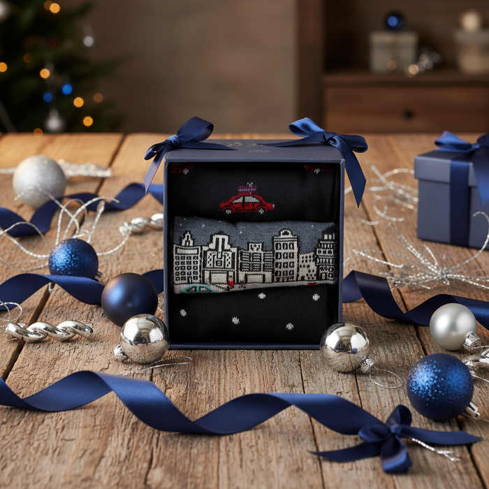 A gift box containing three pairs of men's socks with a Christmas-themed design, including a cityscape. 