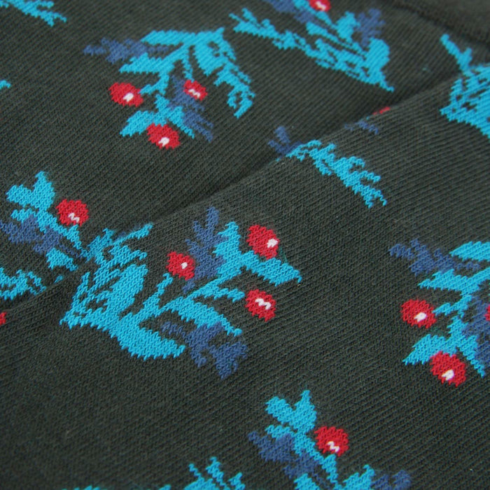 Close-up of a patterned fabric with red and blue holly designs on a green background