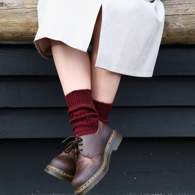 Person wearing maroon wool socks and brown leather shoes sitting on a wooden bench.