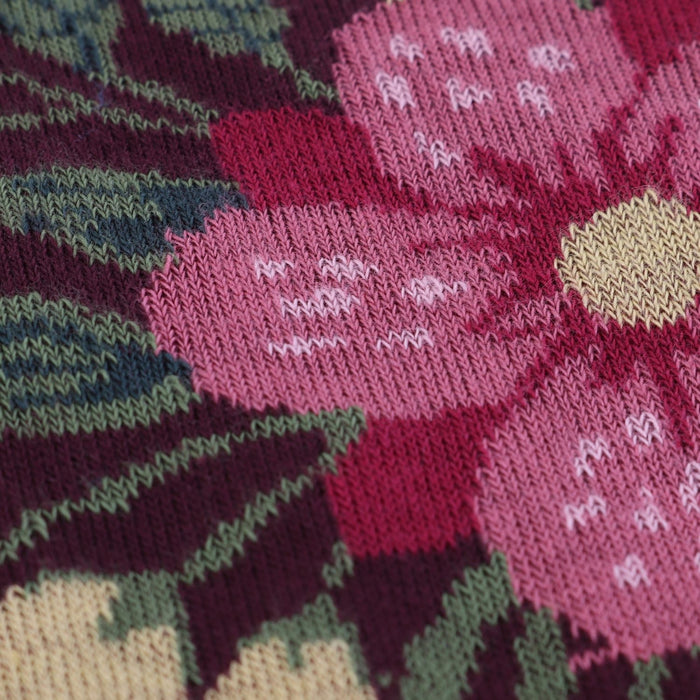 Close-up of a knitted fabric with pink flowers and green leaves.