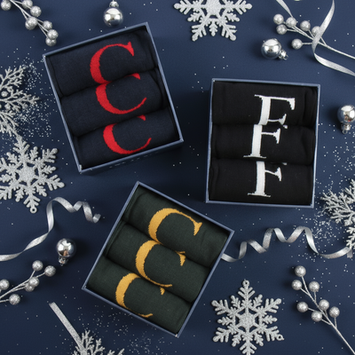 Three pairs of socks in navy boxes with visible brand initials on a blue background with decorative elements.
