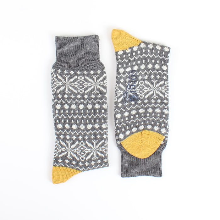 Pair of gray socks with white snowflake pattern and yellow tips on a white background