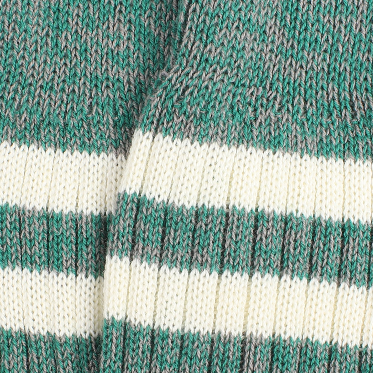 Close-up of a knitted sock made in a green and grey twist with two white stripes.