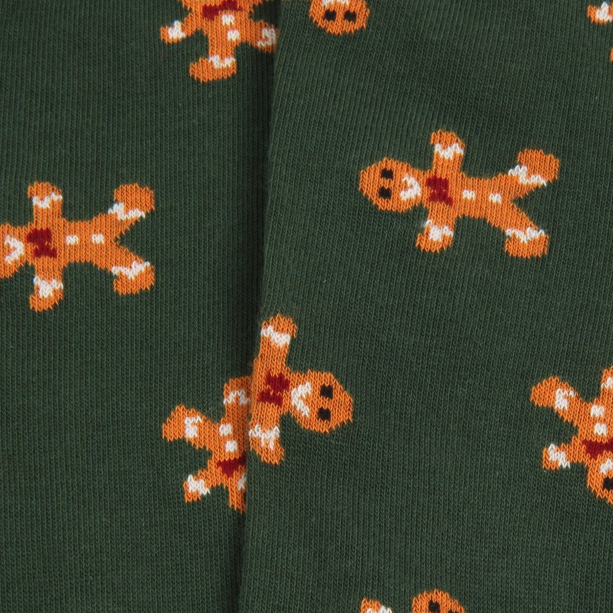 Close-up of dark green knit fabric with an allover pattern of gingerbread cookies in orange, brown, and white.