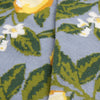 Close-up of a fabric with floral pattern featuring green leaves and white flowers on a blue background.