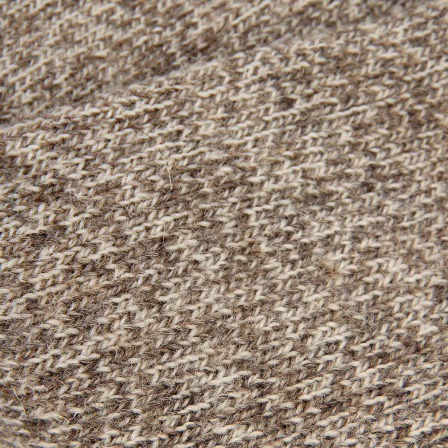 Close-up of a textured knit fabric with a heathered pattern of brown, beige, and cream yarns.