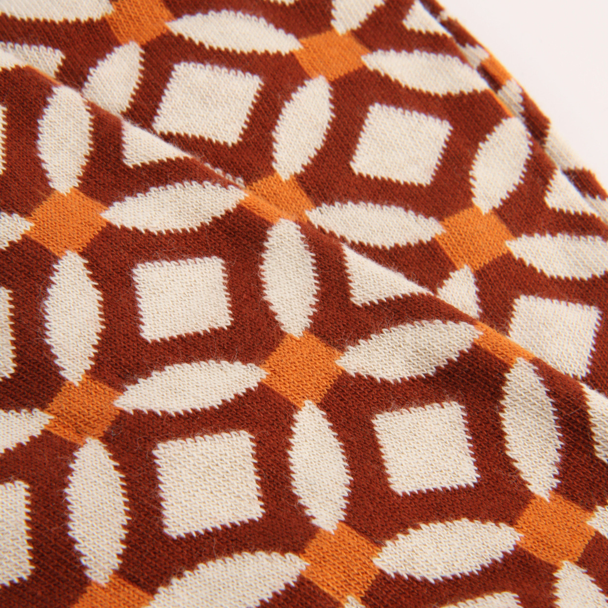 Close-up of a knitted fabric with a geometric pattern in rust brown, cream, and orange.