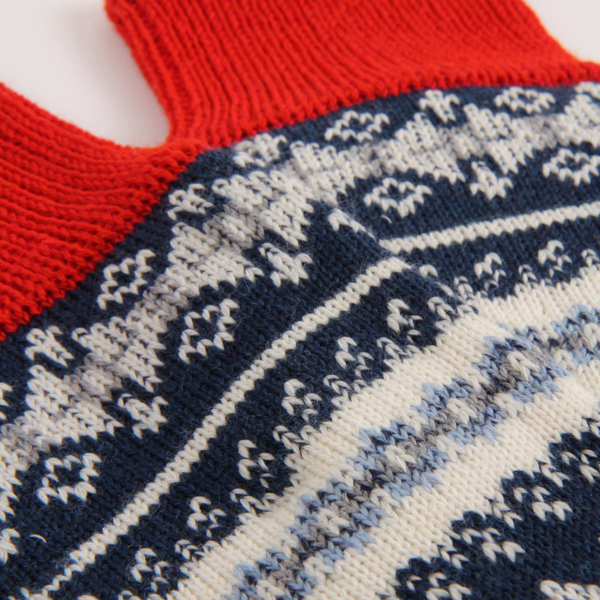 Close-up of a knitted sock showing a red ribbed cuff and a navy, cream, and light blue Fair Isle patterned body.
