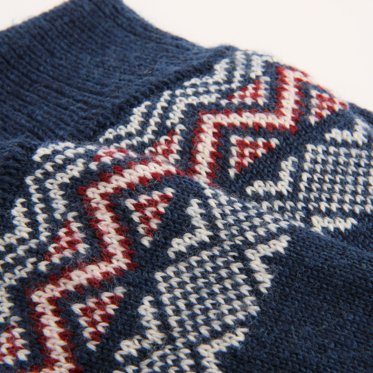 Close-up of a knitted sock showing a Fair Isle pattern in navy blue, cream, and red.