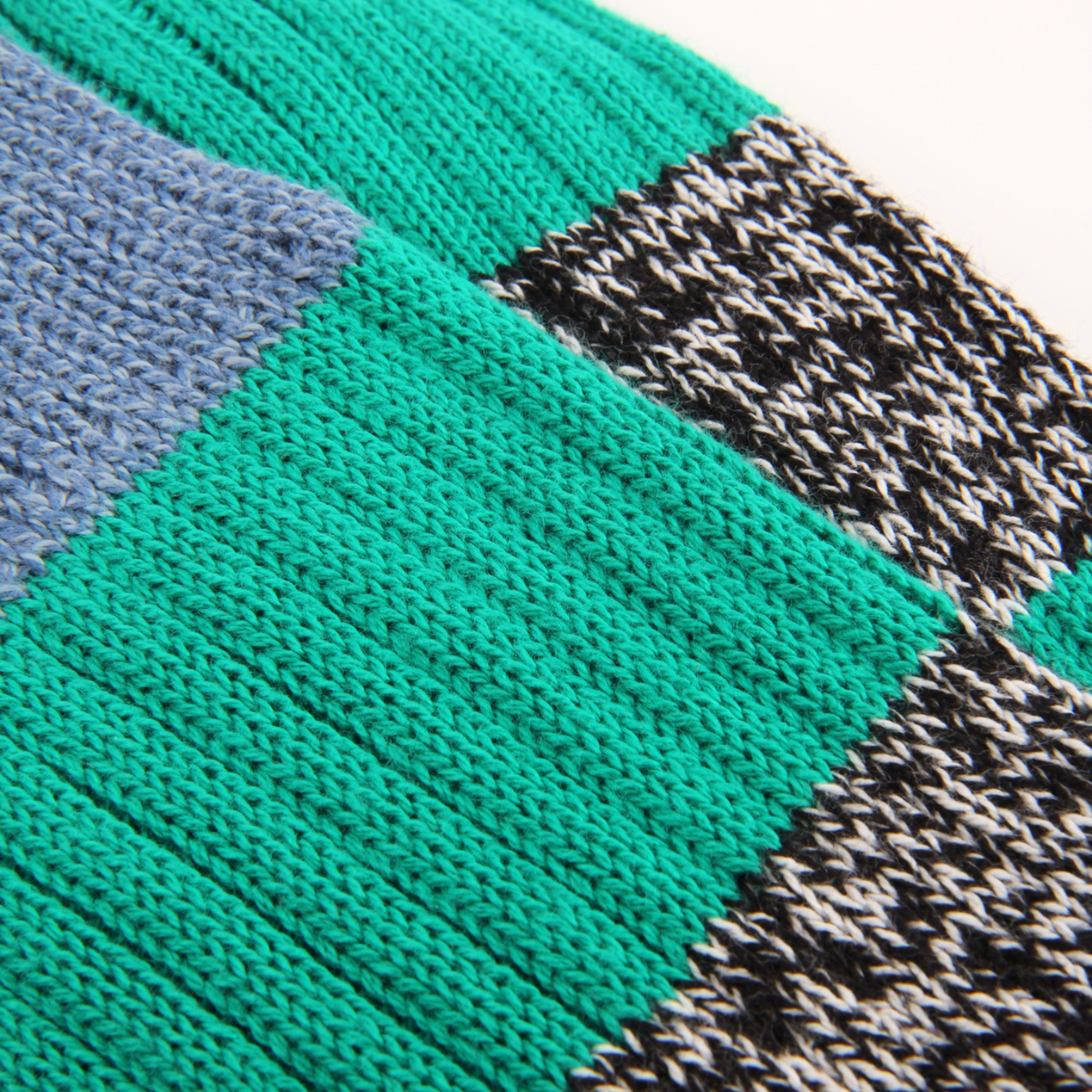 Close-up of a knitted textile with a geometric patchwork pattern, featuring a large teal-green section, a muted blue-gray section, and a black-and-white variegated section.