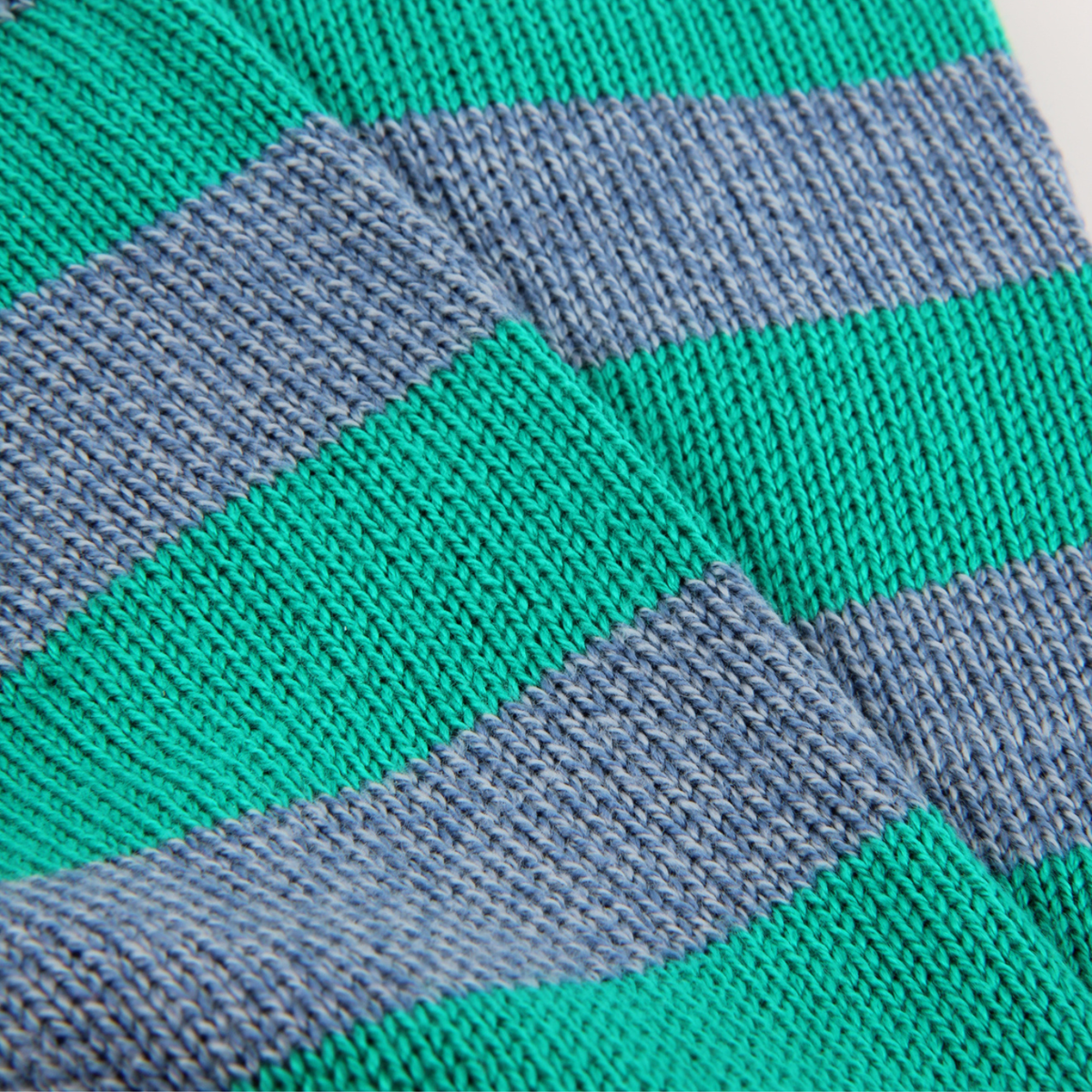 Close-up of a knitted fabric with horizontal stripes in bright green and muted blue-gray, showing the knit texture in detail.