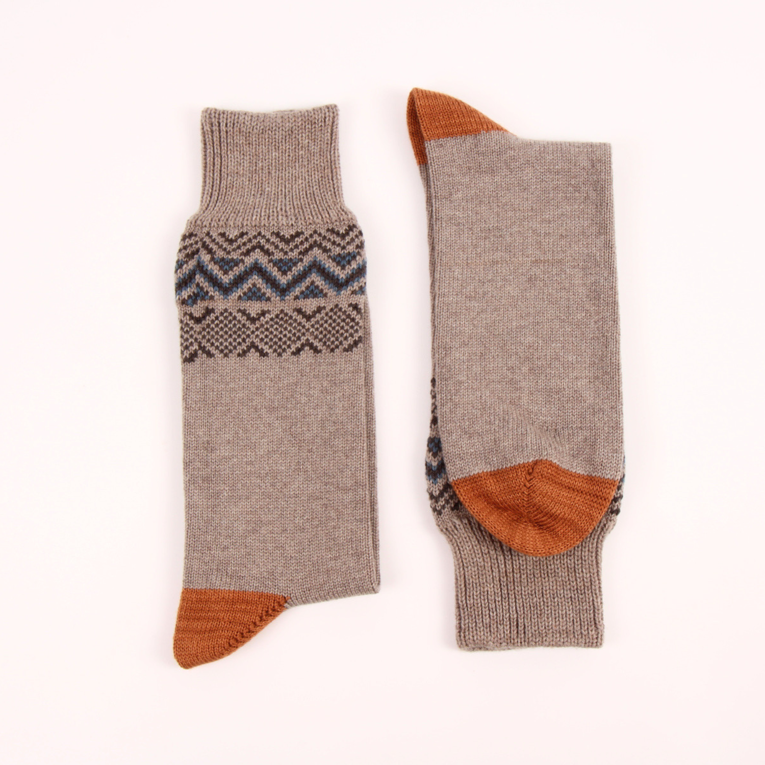 A pair of knit socks laid flat on a light off-white background, showing both the front and back views. The socks are primarily a heathered taupe-brown color with a dark gray and navy blue geometric pattern around the calf and solid rust-orange accents on the toes and heels.