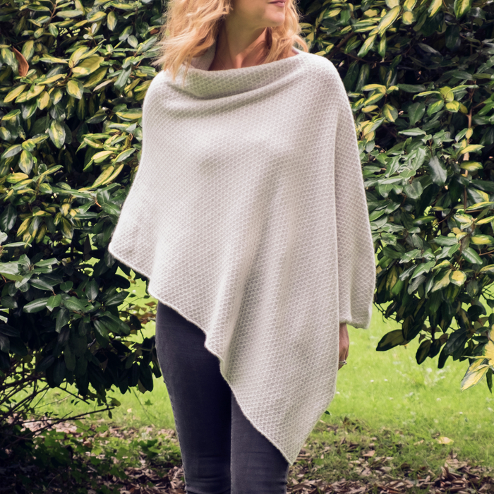 A woman standing outdoors wearing a beige textured cashmere poncho with a honeycomb pattern.