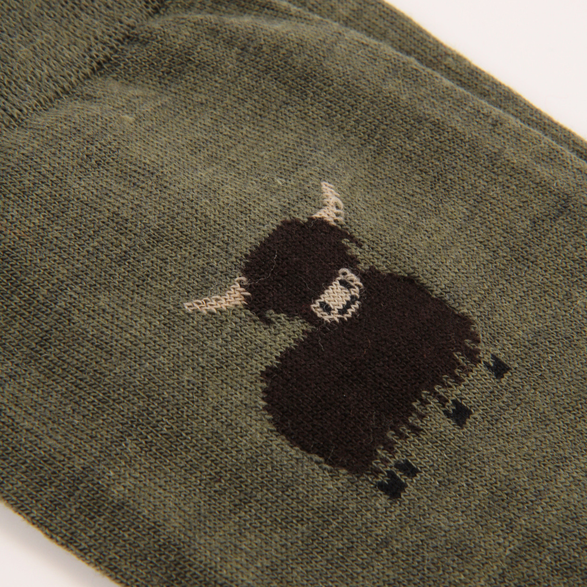 Close-up of an olive green knit sock featuring a black and white embroidered highland cow motif.