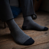 Gray socks with black toes and cuffs worn by a person sitting on a wooden floor.
