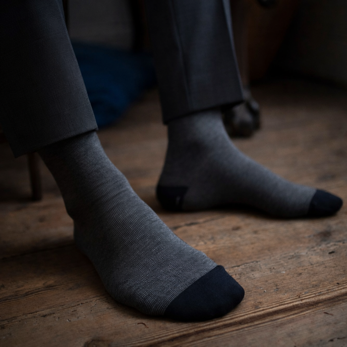 Gray socks with black toes and cuffs worn by a person sitting on a wooden floor.