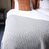 Gray cable knit blanket on a bed with colorful pillows