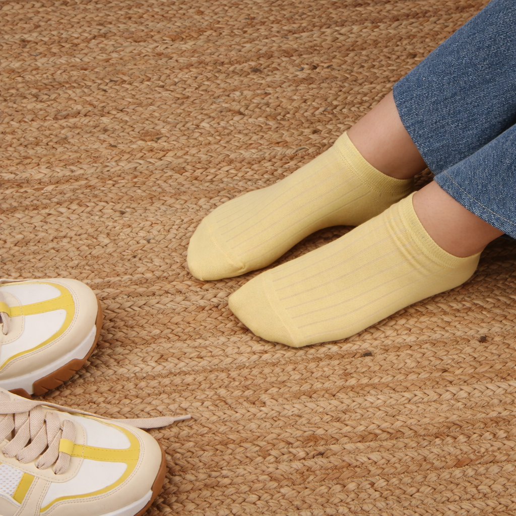 Yellow socks worn with white sneakers on a textured brown floor.