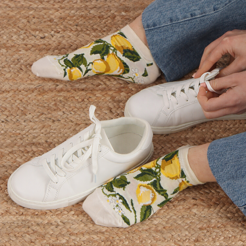 Person wearing white sneakers and lemon-patterned socks on a carpeted floor.