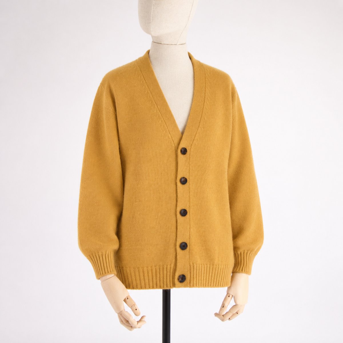 A mustard yellow knit cardigan sweater displayed on a cream-colored mannequin torso with wooden hands, set against a plain white background.