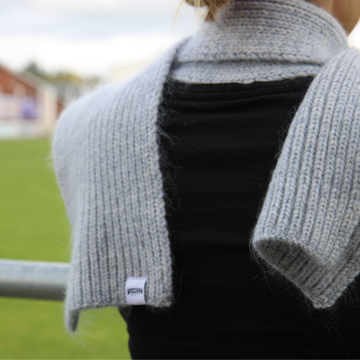 Person wearing a grey knitted scarf over a black top with a blurred outdoor background