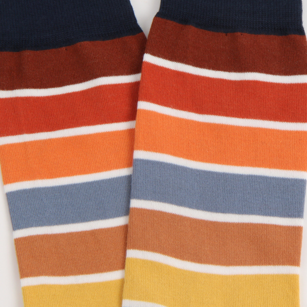 A close-up of a pair of striped knit socks with horizontal bands of navy, rust, orange, light blue, tan, and yellow on a white background.