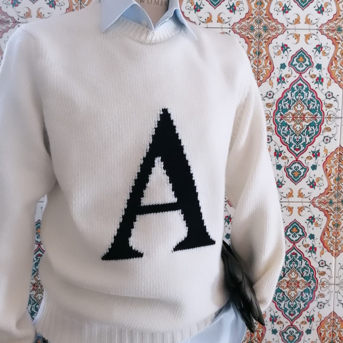 White sweater with a black letter 'A' on a patterned background