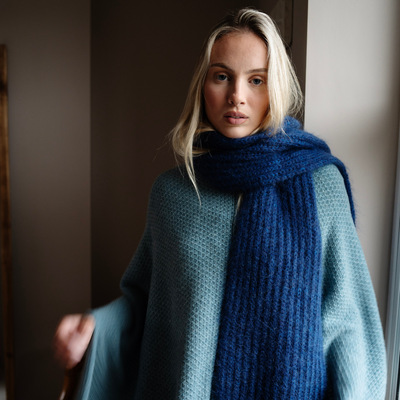 Woman wearing a blue scarf and teal coat indoors