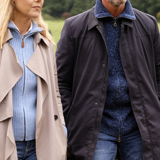 Two people wearing matching blue knitted zip cardigans and coats outdoors.