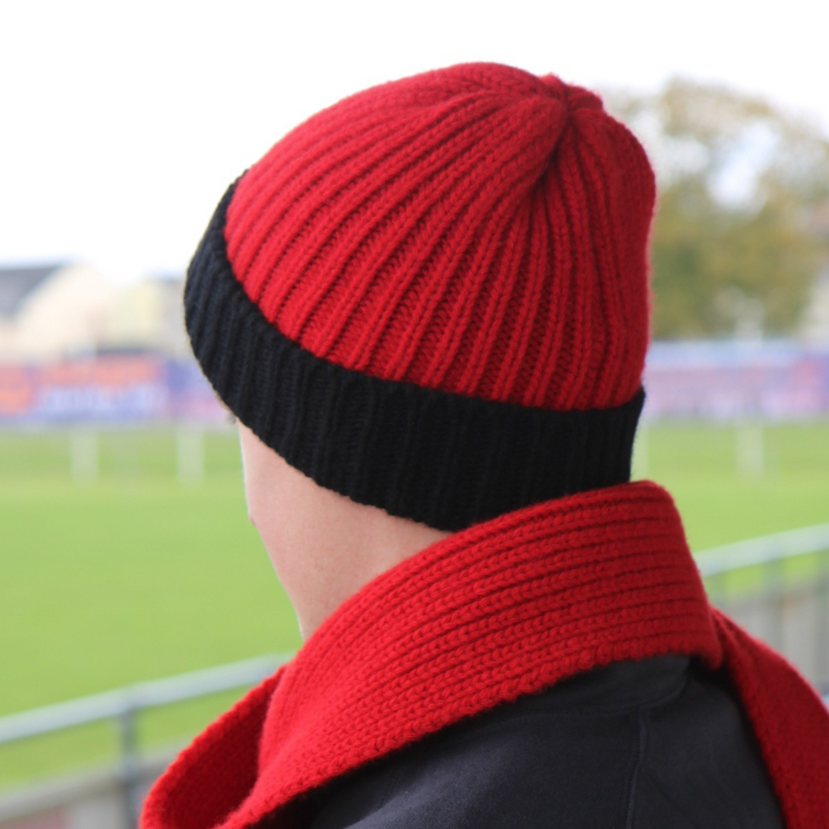 Person wearing a red and black knit hat and scarf with a blurred sports field background