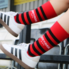 Red and black striped socks with 'WREXHAM' branding worn with white sneakers.