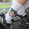 Person wearing white socks with a logo and black Adidas shoes in a stadium setting.